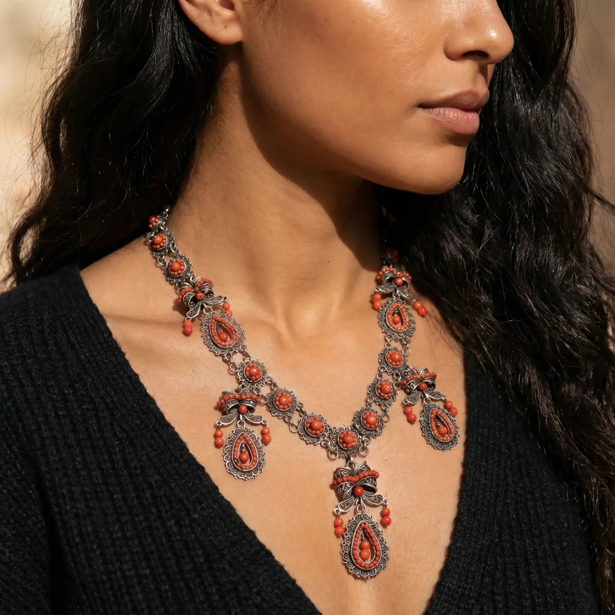 An ornate coral and silver necklace with intricate filigree designs and teardrop-shaped pendants.