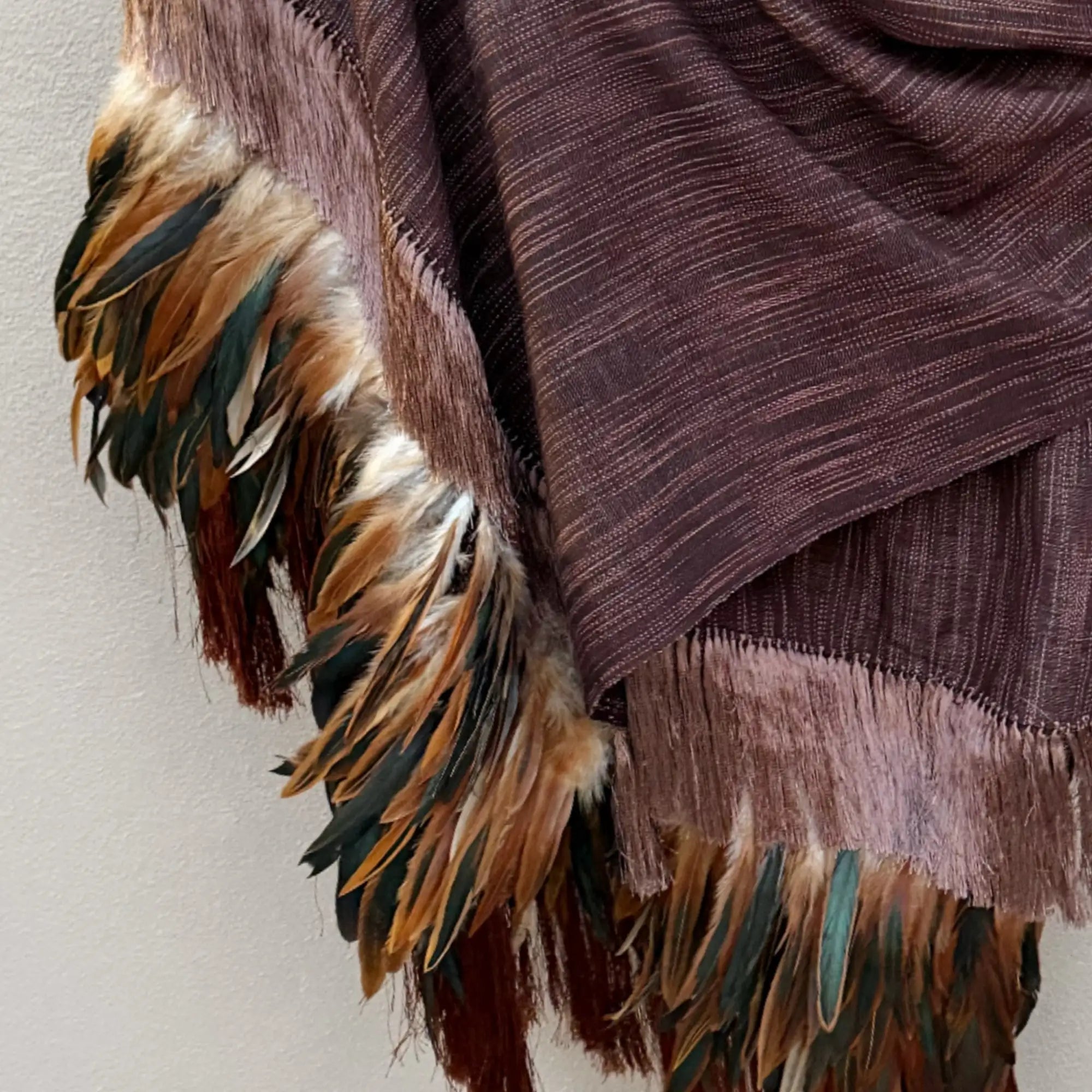 A plush, textured maroon scarf adorned with a vibrant fringe of multicolored feathers in shades of brown, green, and gold.
