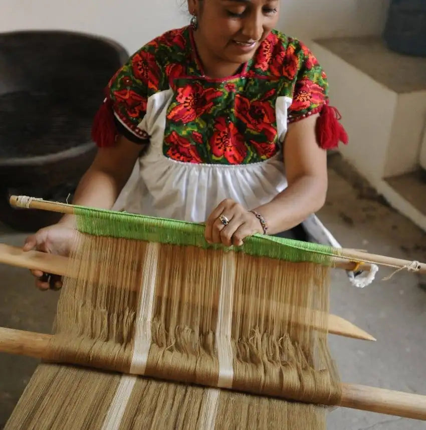 A traditional wooden loom with natural-colored threads and a vibrant green warp thread.