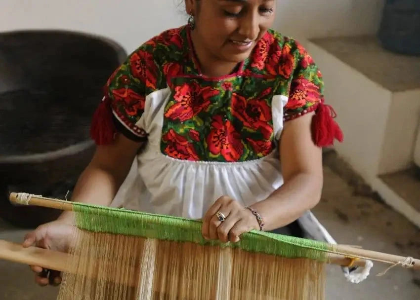 A traditional wooden loom with natural-colored threads and a vibrant green warp thread.