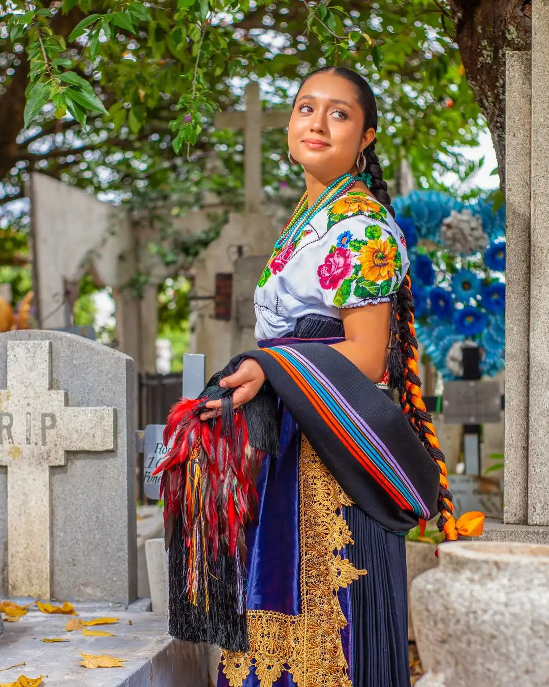 Woman wearing a traditional embroidered blouse with colorful floral patterns and a dark blue skirt adorned with gold lace trim.
